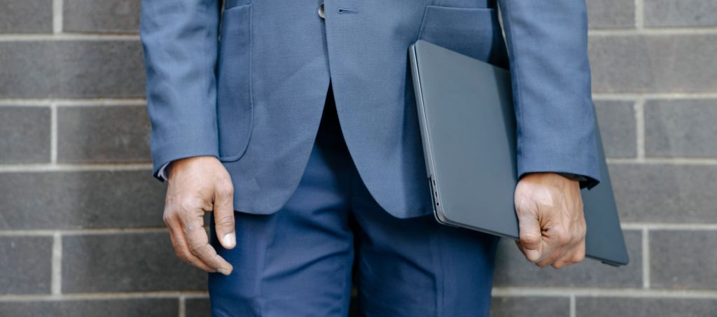 Dominating Local Search: How to Scale 'Service in City' Searches for Your WordPress Site 1 Close-up of a businessman in a blue suit holding a laptop against a brick wall.