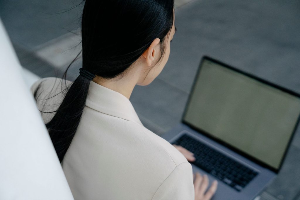 Back view of a woman using a laptop in an outdoor setting, focused on work.