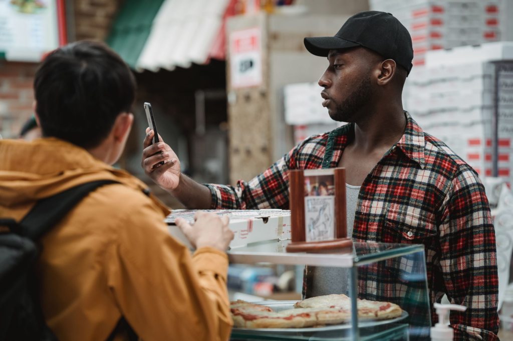 Abandoned Cart Recovery: How to Win Back Customers with Personalized Outreach 1 Two people interacting at a pizzeria counter, one holding a smartphone.
